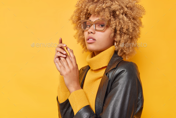 Sideways Shot Of Serious Curly Haired Woman Keeps Hands Together Looks